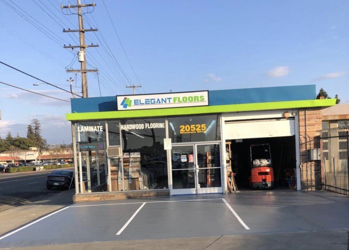 Exterior of Elegant Flowers shop with a blue and green awning, storefront, and open garage door revealing a forklift.