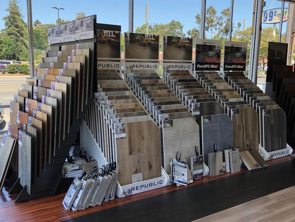 Display of flooring samples in a showroom; various colors and textures are visible, with signage above each row.