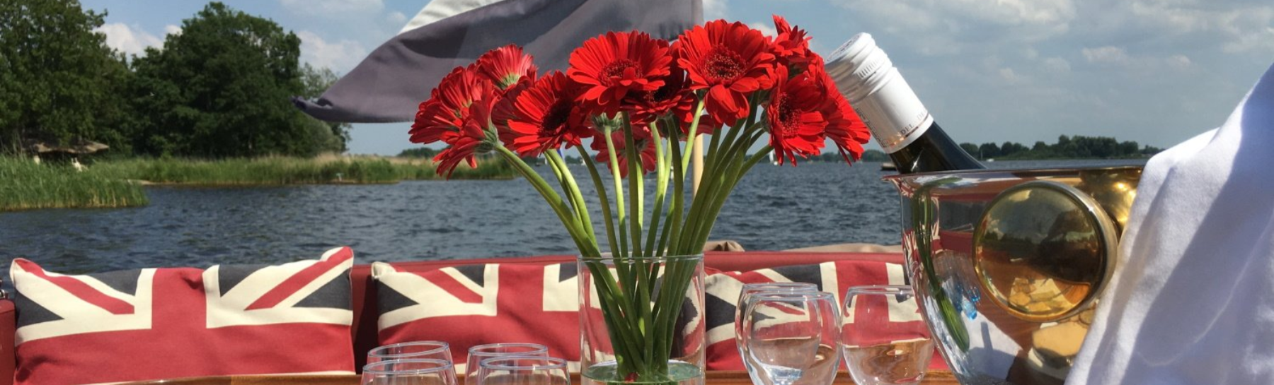 Een vaas met rode bloemen op een tafel met kussens met de Britse vlag, tegen een achtergrond van water en groen.