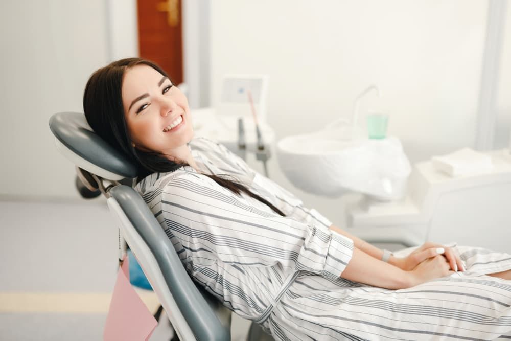 A Woman Is Sitting in A Dental Chair and Smiling — Cane to Coast Dentures in Moranbah, QLD
