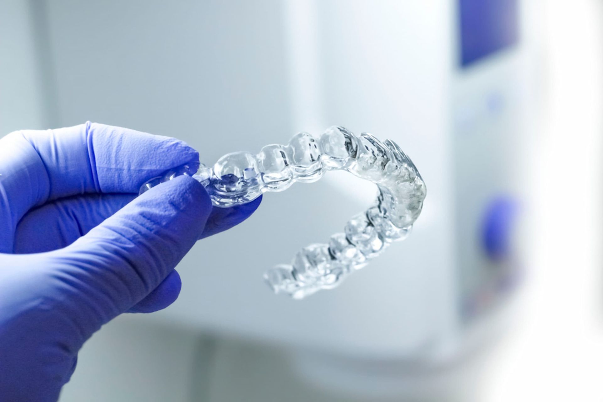 A Person Wearing Blue Gloves Is Holding a Clear Brace in Their Hand — Cane to Coast Dentures in Proserpine, QLD