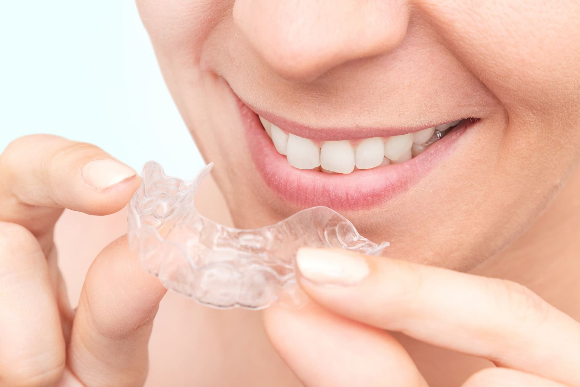 A Woman Is Holding a Clear Retainer in Front of Her Teeth — Cane to Coast Dentures in Moranbah, QLD