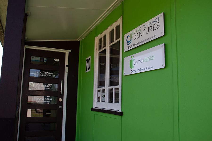 A Green Building with Two Signs on The Side of It — Cane to Coast Dentures in Sarina, QLD