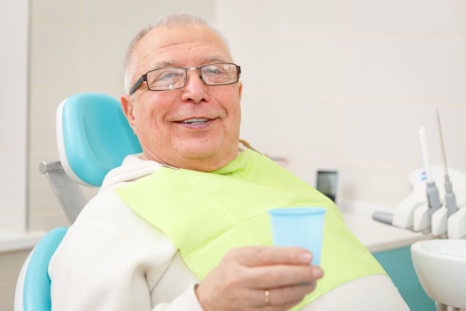 An Elderly Man Is Sitting in A Dental Chair Holding a Cup of Water — Cane to Coast Dentures in Sarina, QLD