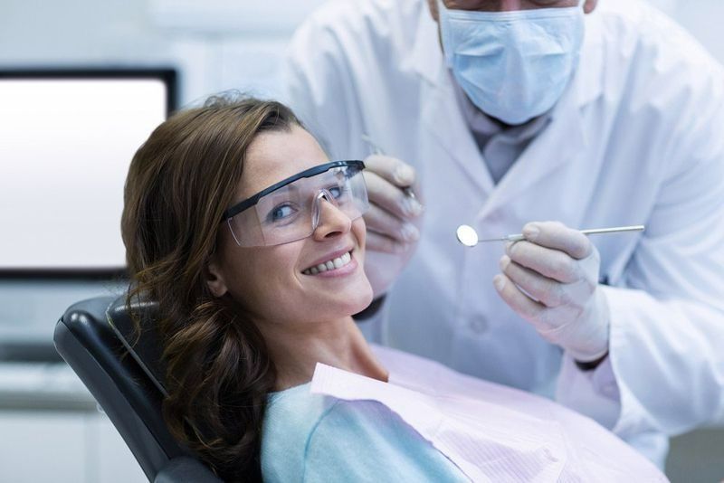A Woman Is Sitting in A Dental Chair While a Dentist Examines Her Teeth — Cane to Coast Dentures in Sarina, QLD