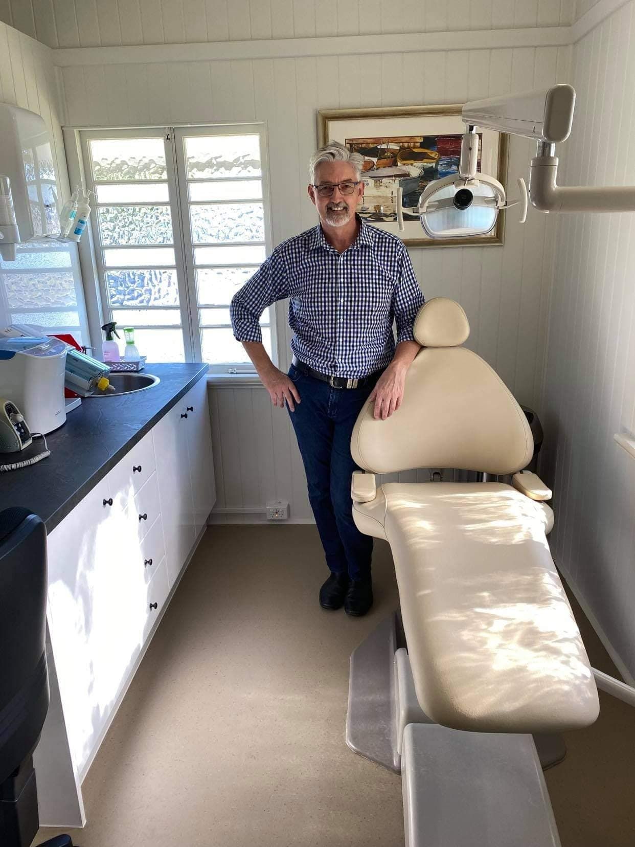 A Man Is Standing Next to A Dental Chair in A Dental Office — Cane to Coast Dentures in Sarina, QLD