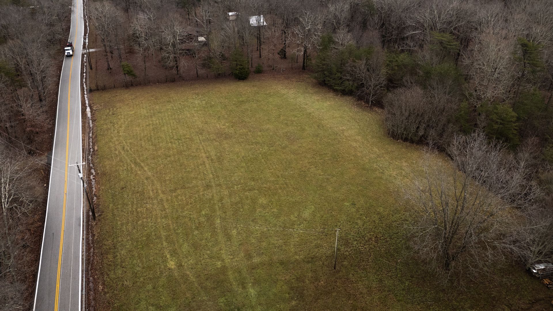 Overhead view of a grassy field next to a road, surrounded by trees.