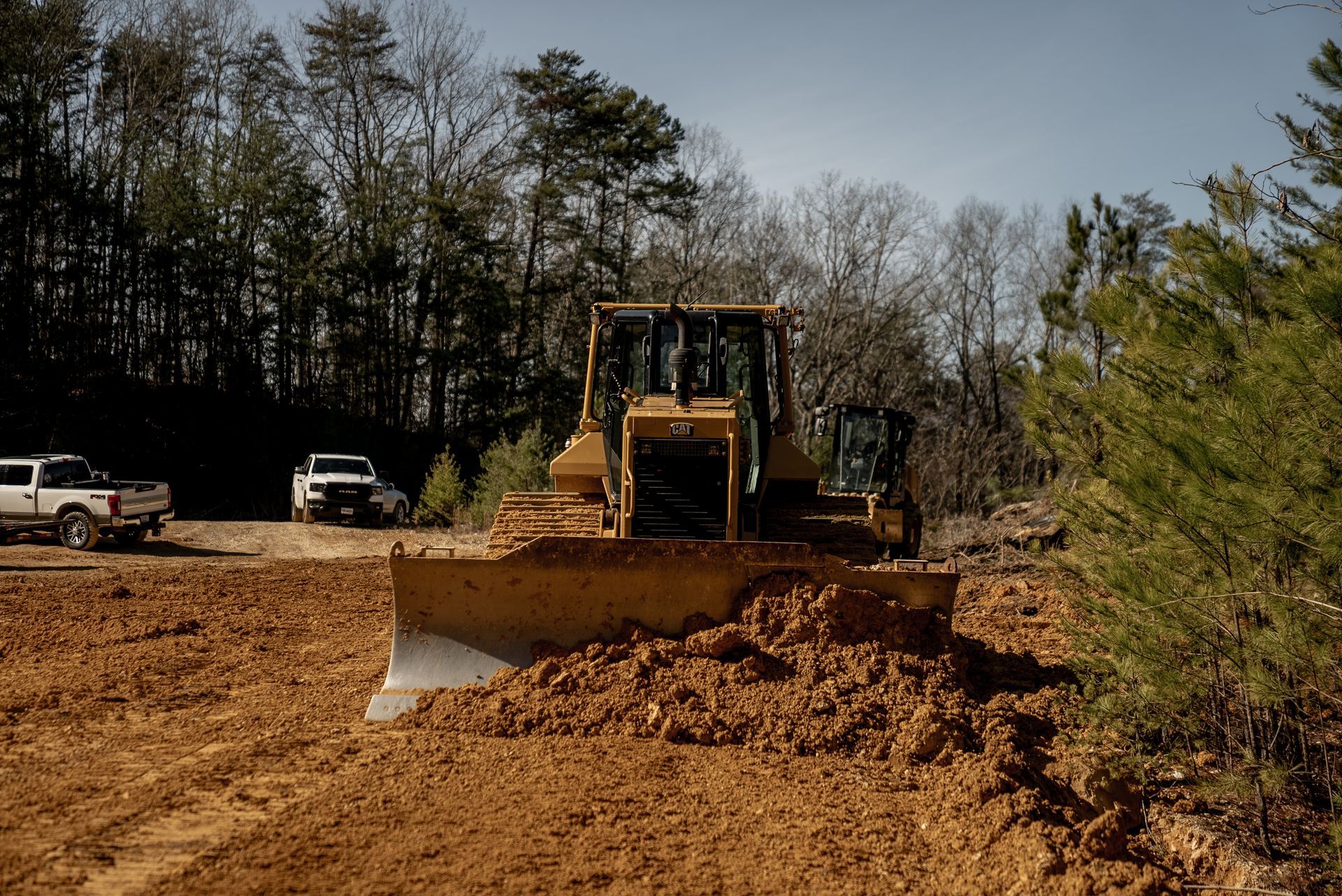 A bulldozer pushing dirt on a construction site. Two white trucks are parked nearby.