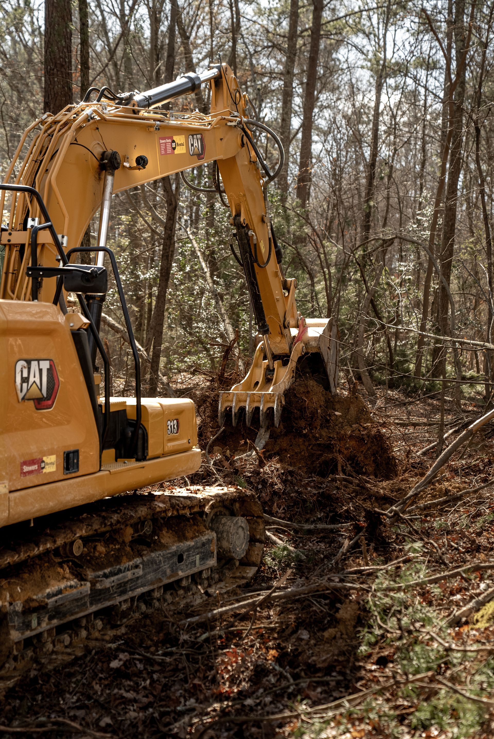 Yellow excavator clearing debris in a wooded area.