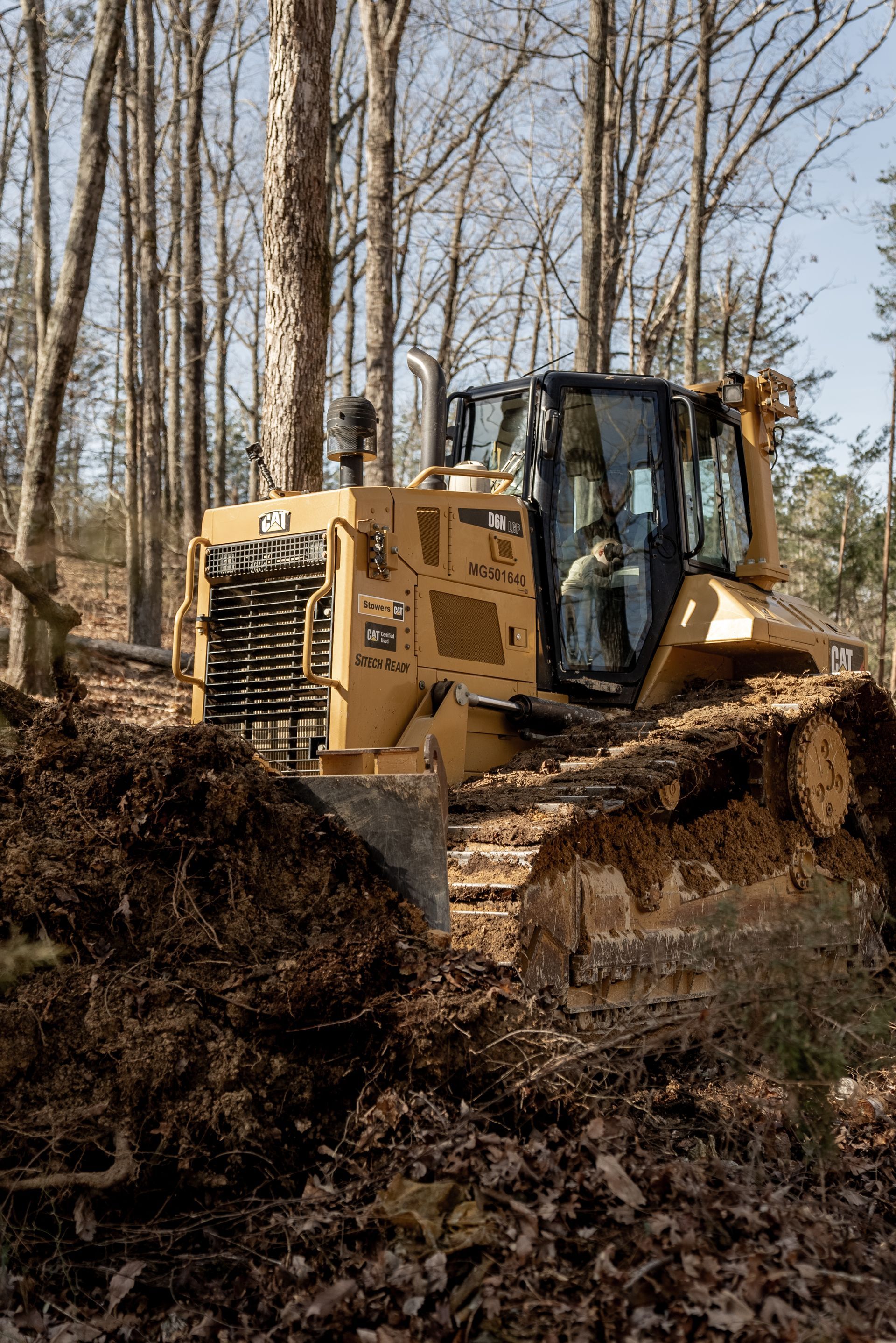 Yellow bulldozer clearing dirt and debris in a wooded area.