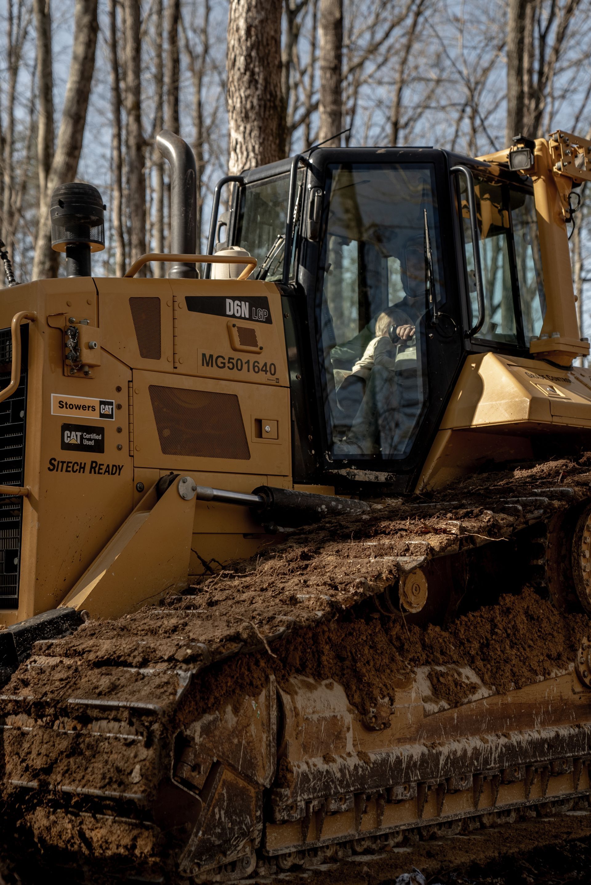 Yellow bulldozer in a muddy forest, tracks visible. Operator visible inside the cab.