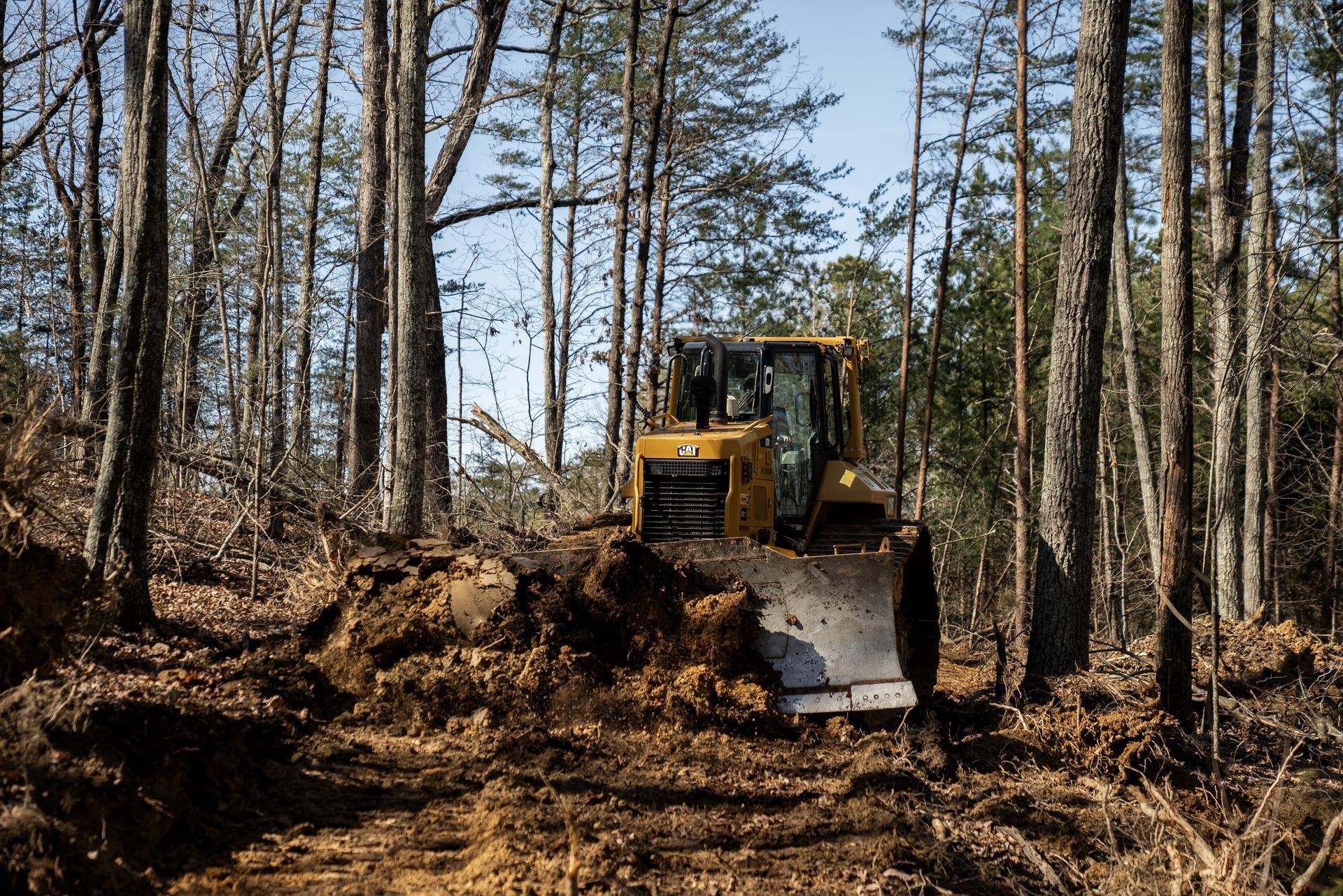 Yellow bulldozer clearing land in a forest, pushing dirt and debris.