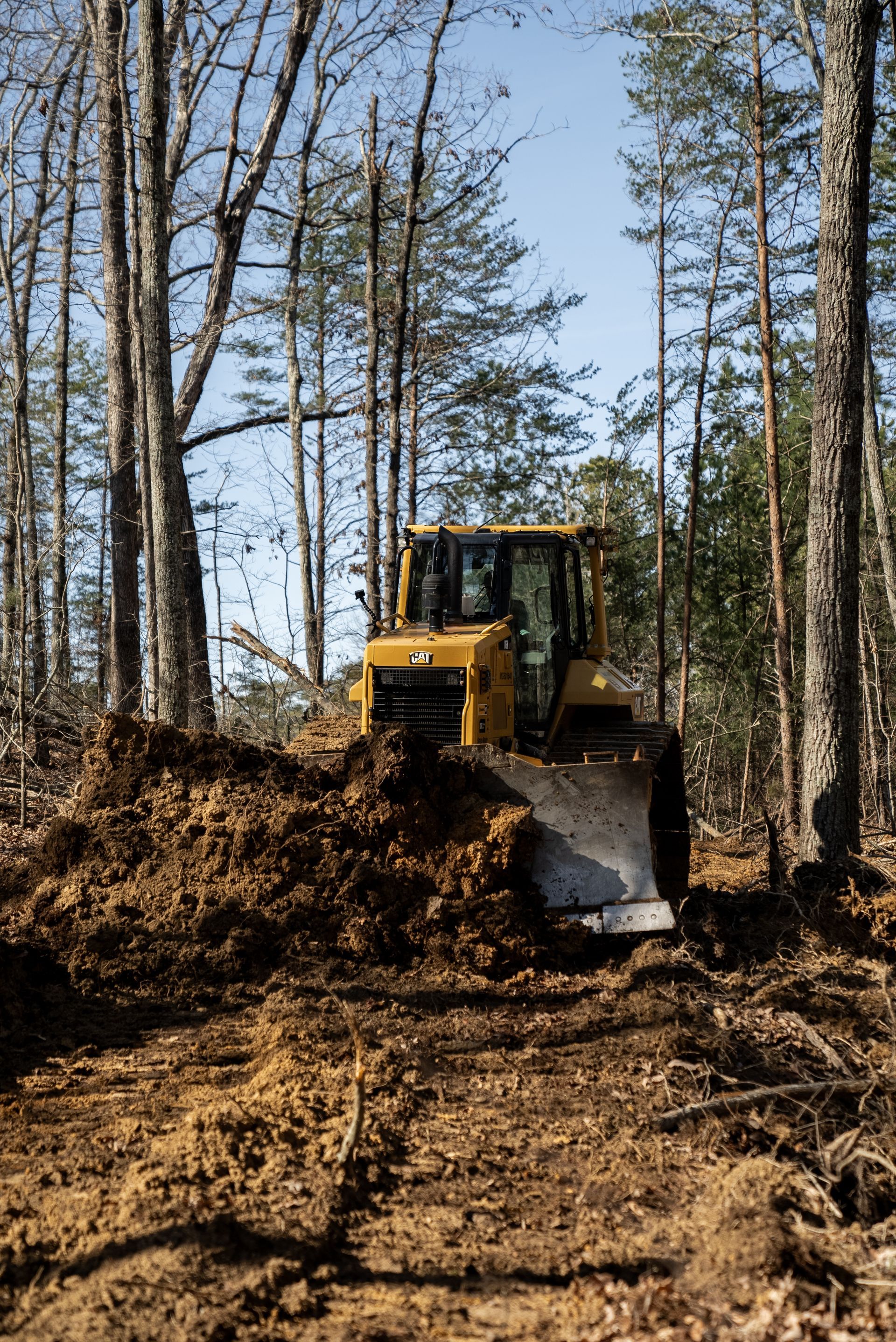 A yellow bulldozer pushing dirt in a forest clearing.