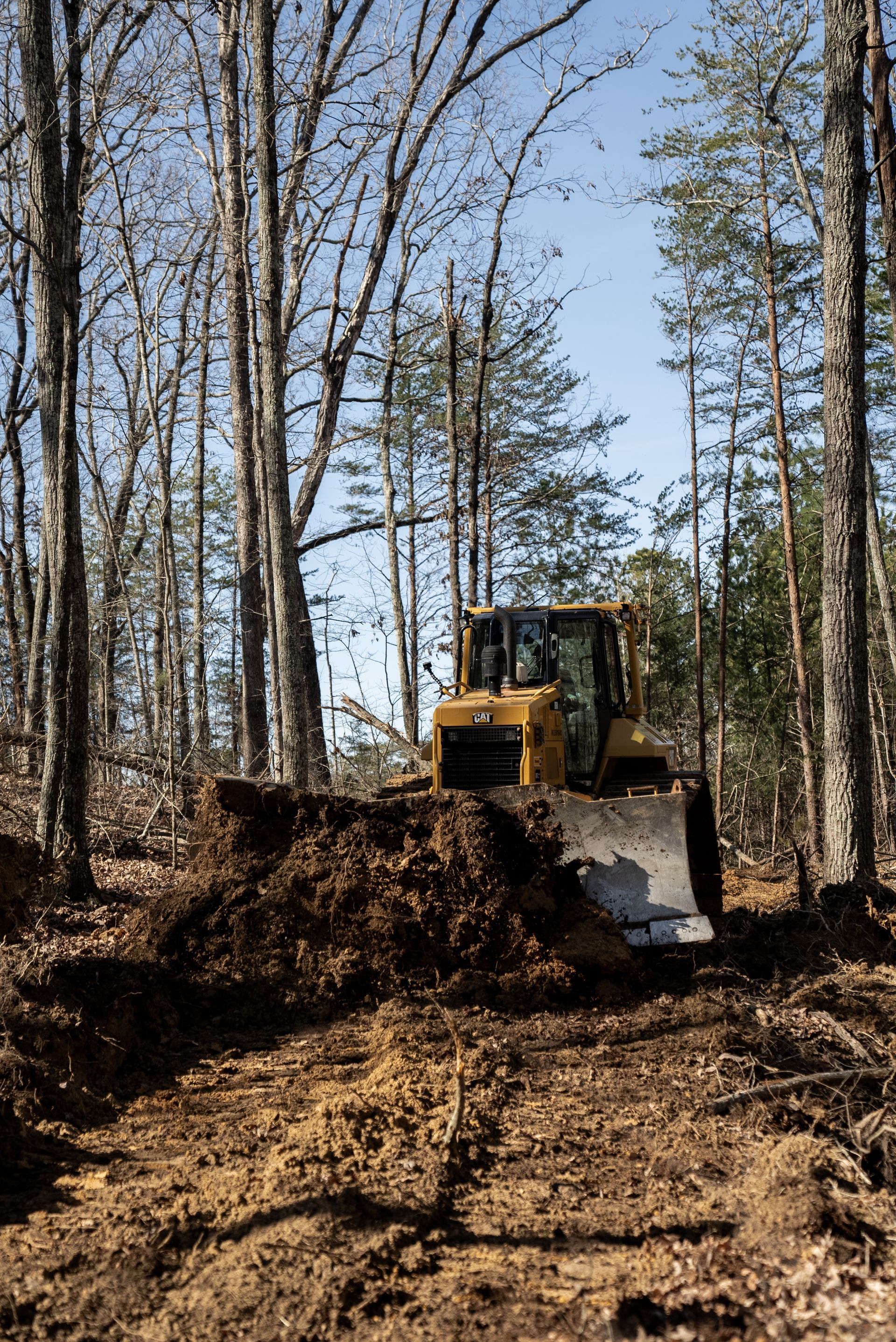 Yellow bulldozer clearing land in a forest, pushing dirt and debris.