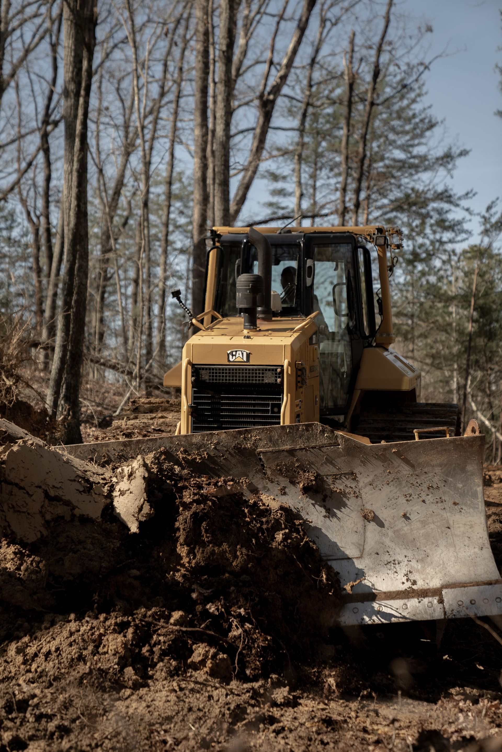 Yellow Caterpillar bulldozer pushing dirt in a wooded area.