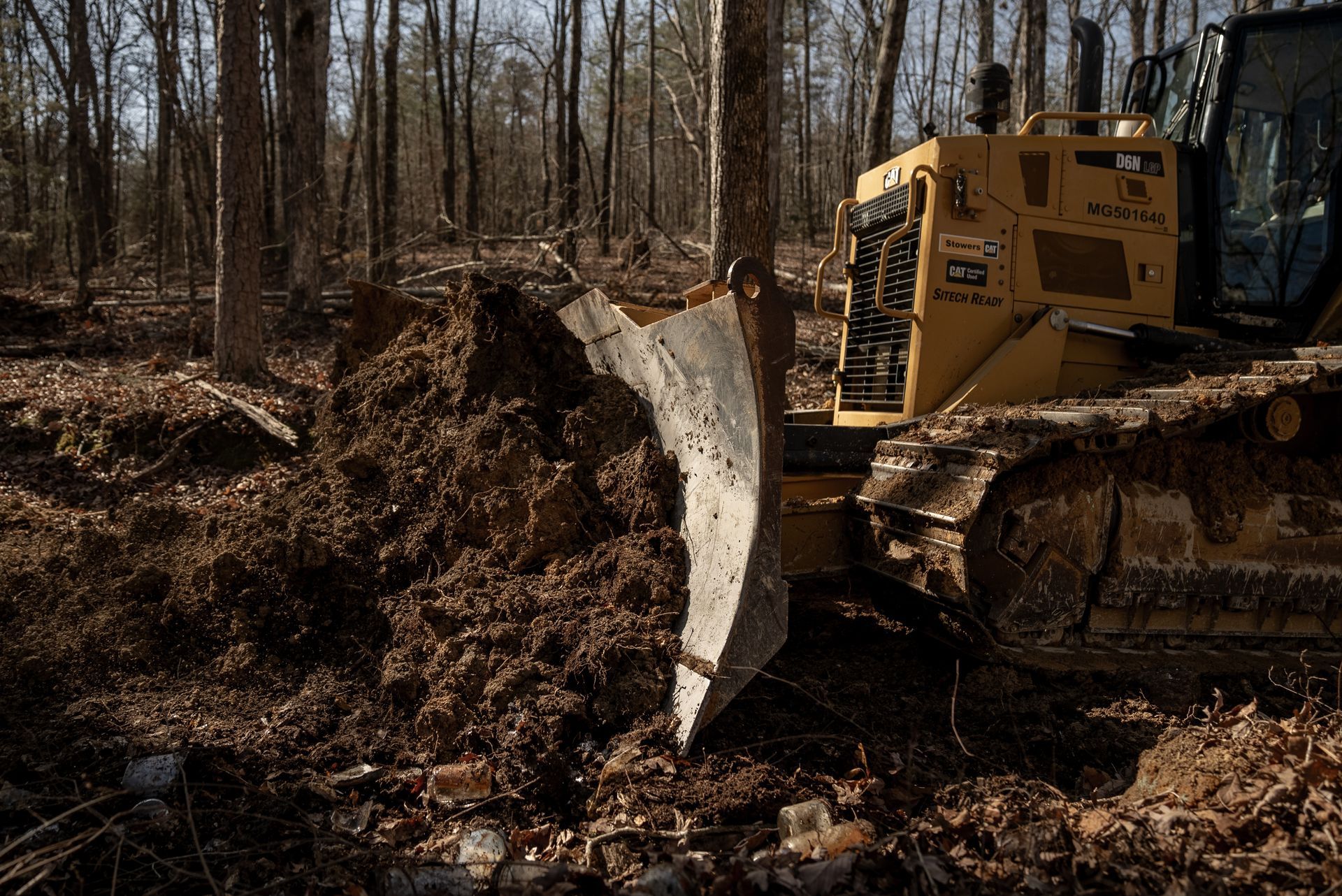 Bulldozer clearing a forest, pushing dirt and debris, sunny day.
