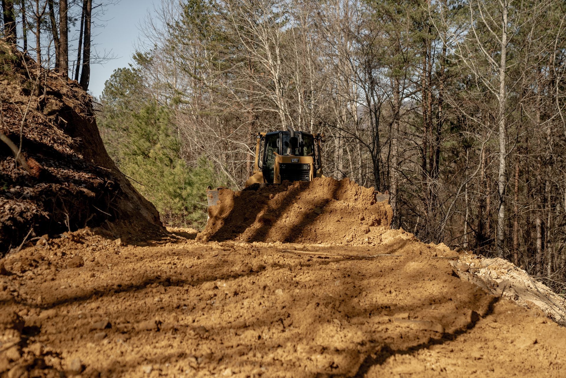 A dirt-covered vehicle on a man-made mound in a wooded area. Trees and blue sky are visible in the background.