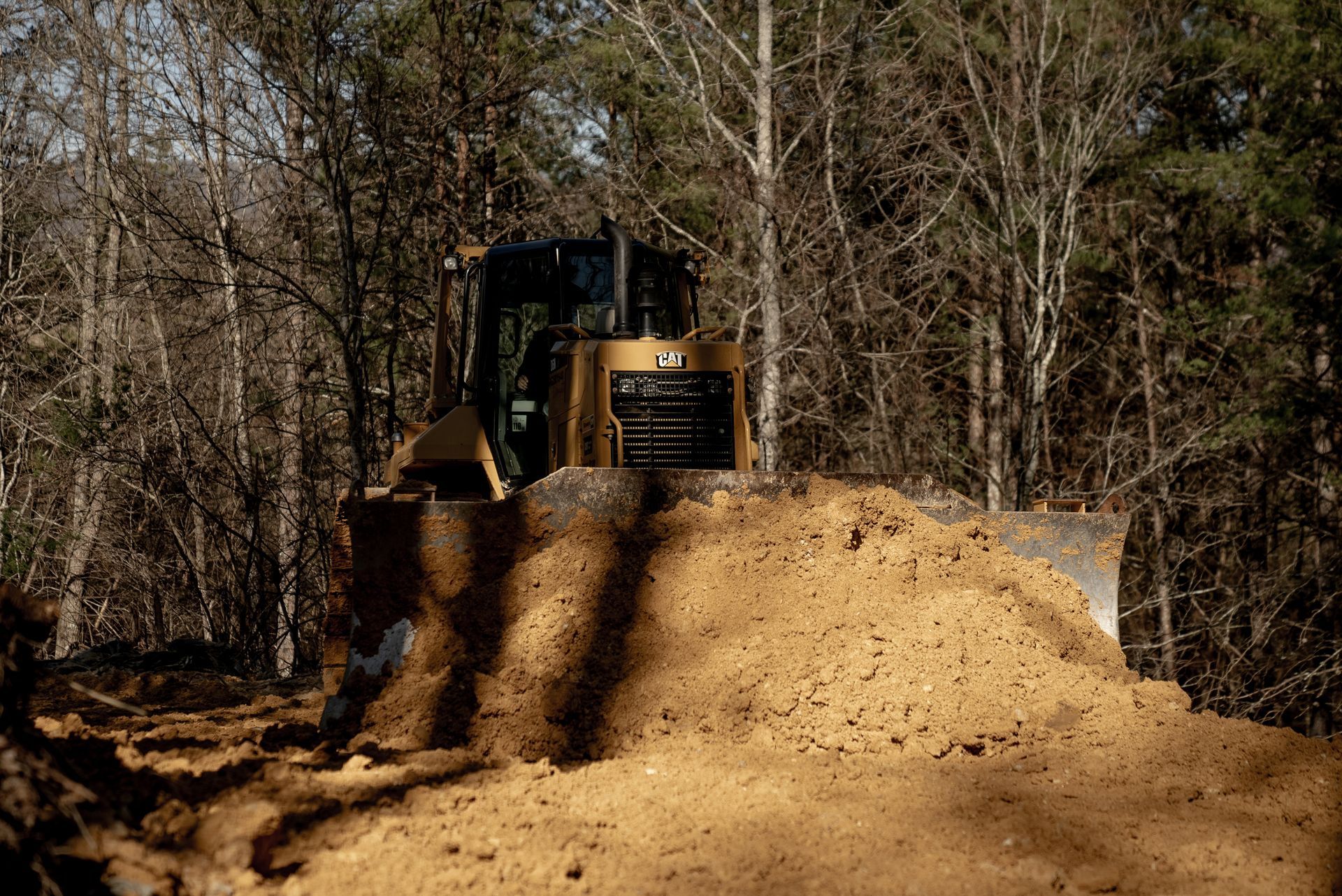 Bulldozer pushing dirt; trees in background.