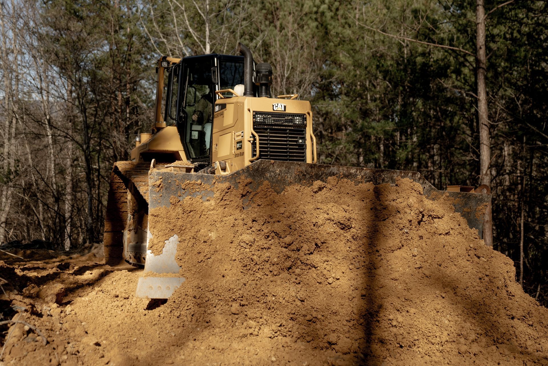 Yellow bulldozer pushing a pile of brown earth in a wooded area.