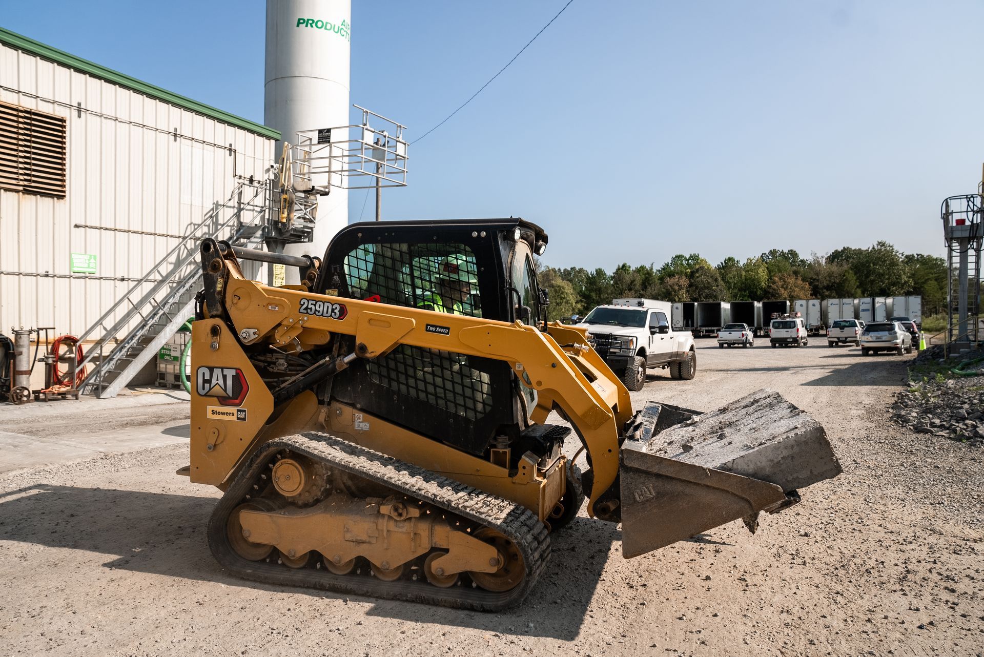 Yellow Caterpillar skid steer with full bucket, in industrial yard.