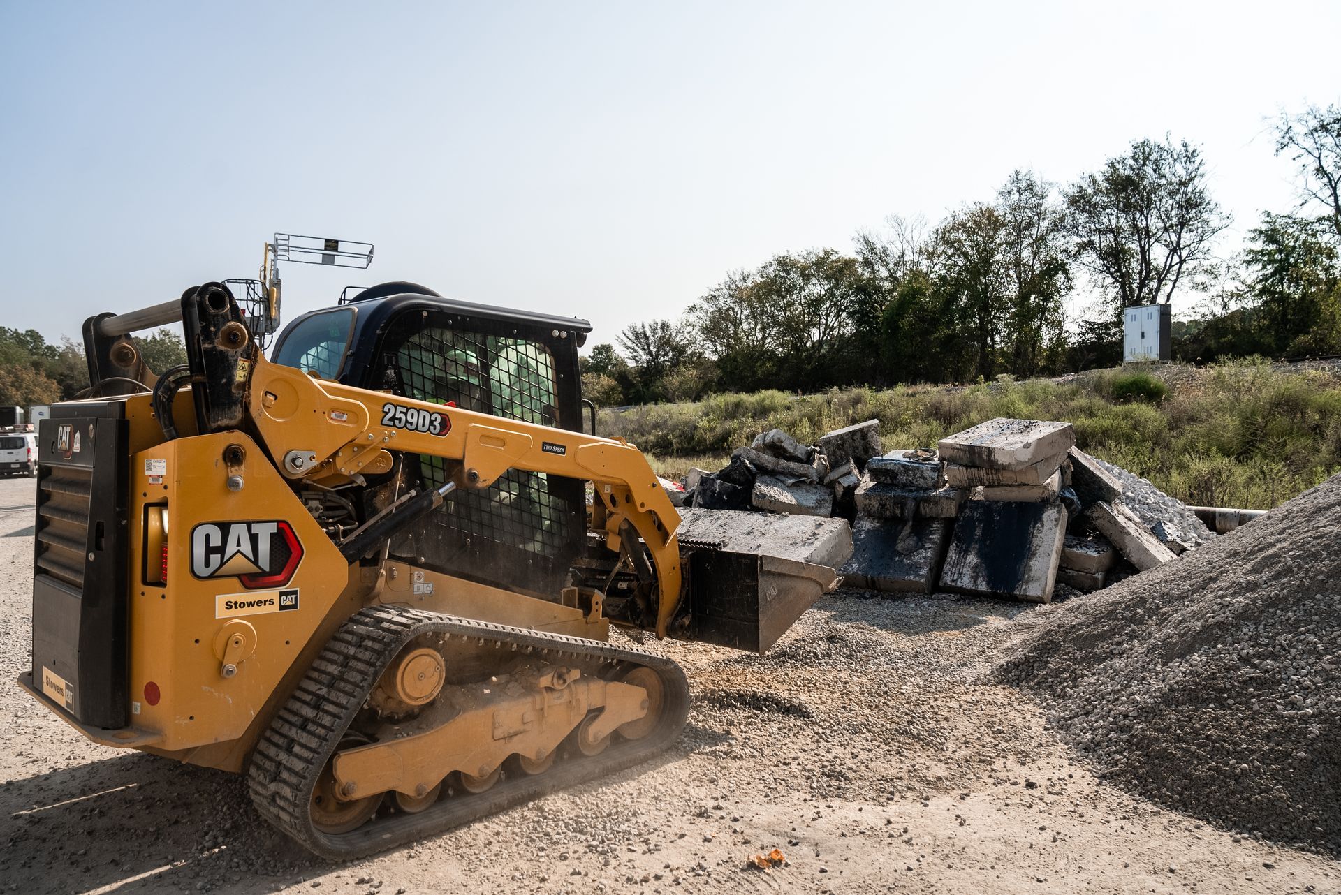 Yellow CAT skid steer at a construction site with broken asphalt and a pile of gravel.