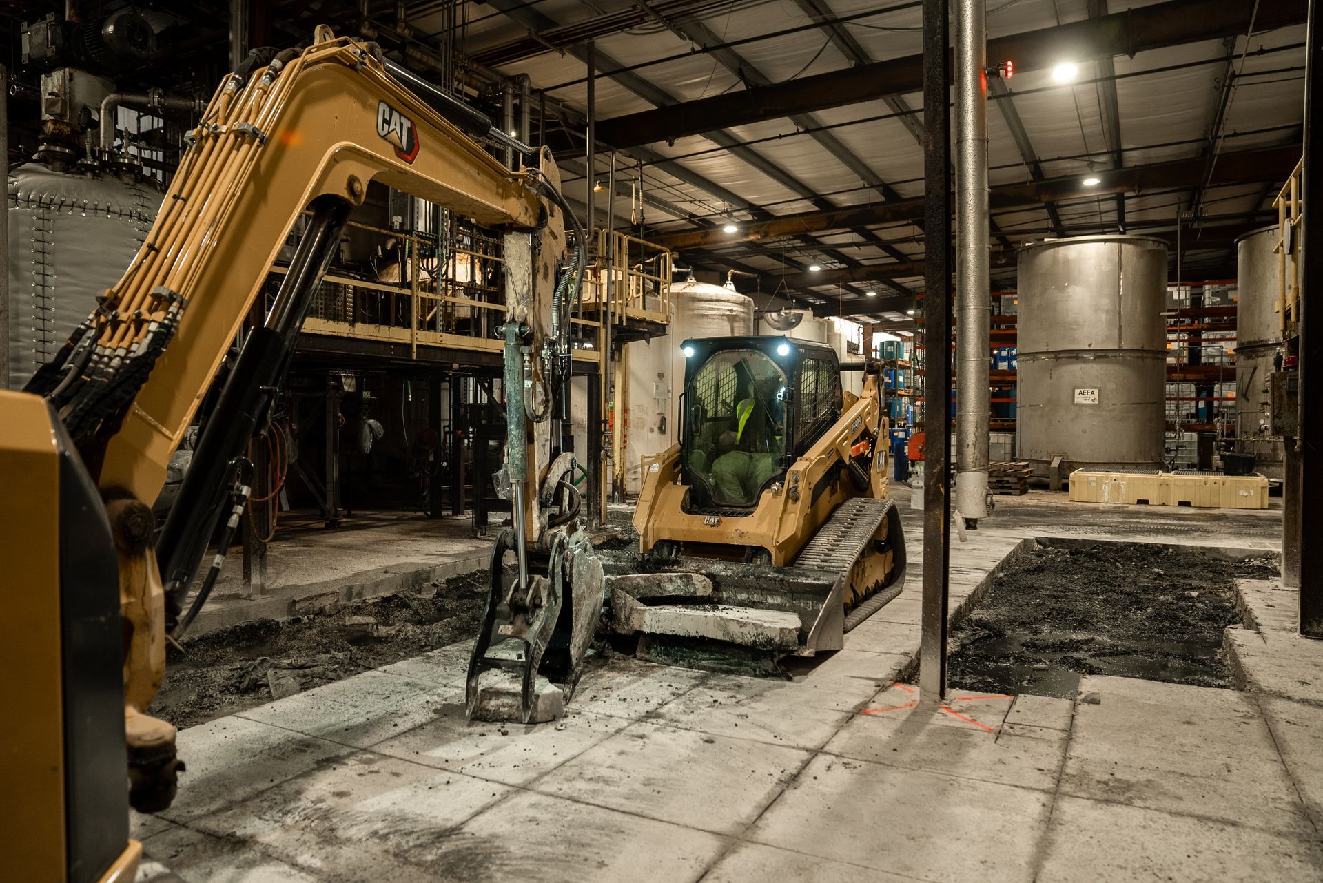 Yellow Caterpillar excavator and skid steer in industrial building. Construction is in progress.