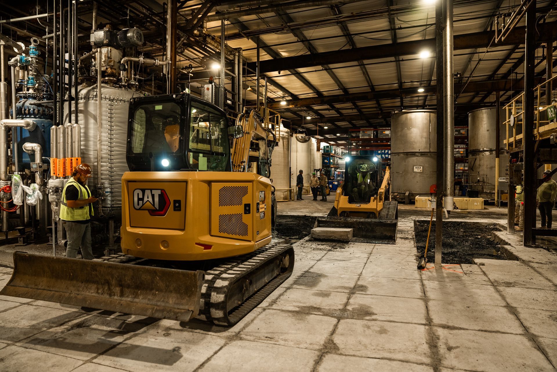 Yellow CAT excavator inside industrial building, worker in hard hat.