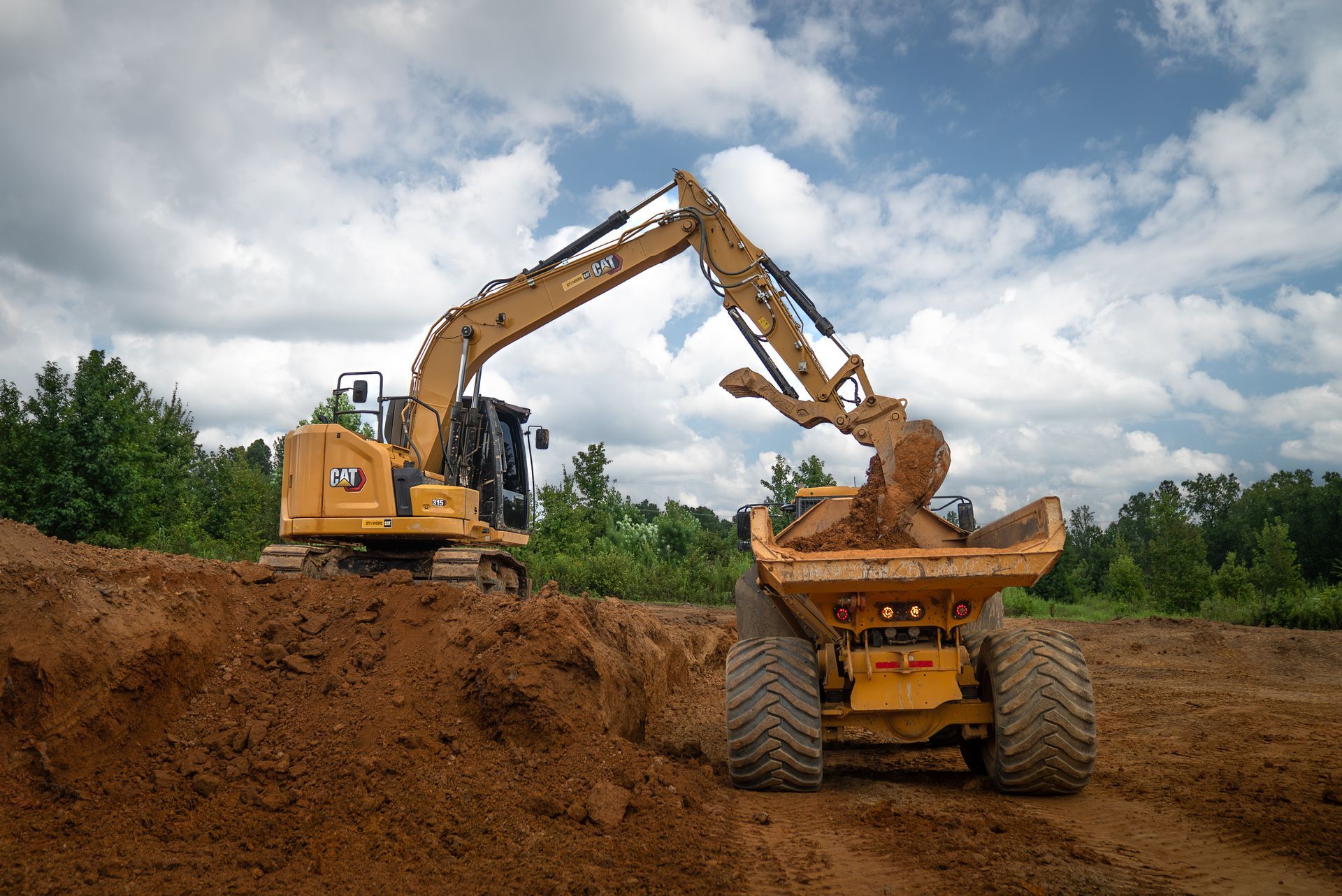Yellow excavator loading dirt into a dump truck at a construction site. Cloudy sky.