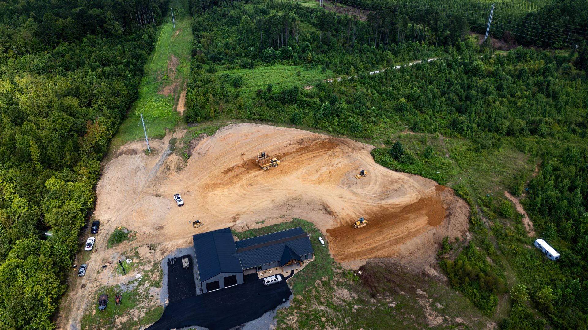 Aerial view of a construction site clearing land; several buildings and heavy machinery visible in a wooded area.