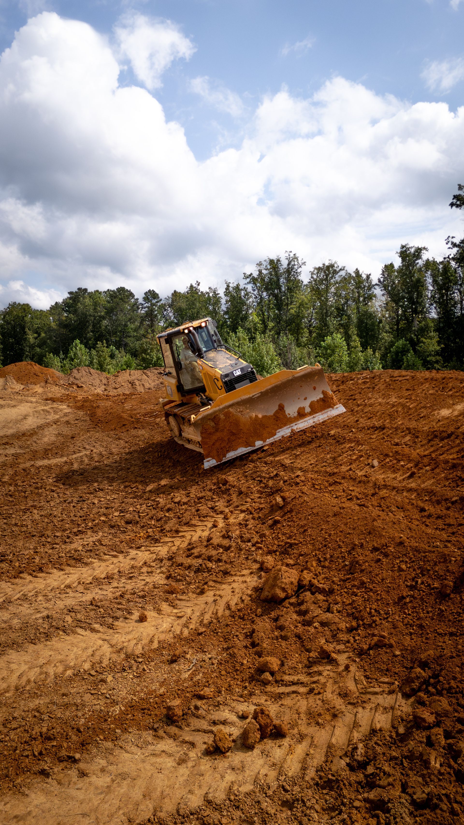 Dozer on a mound of dirt under a cloudy sky, clearing land.