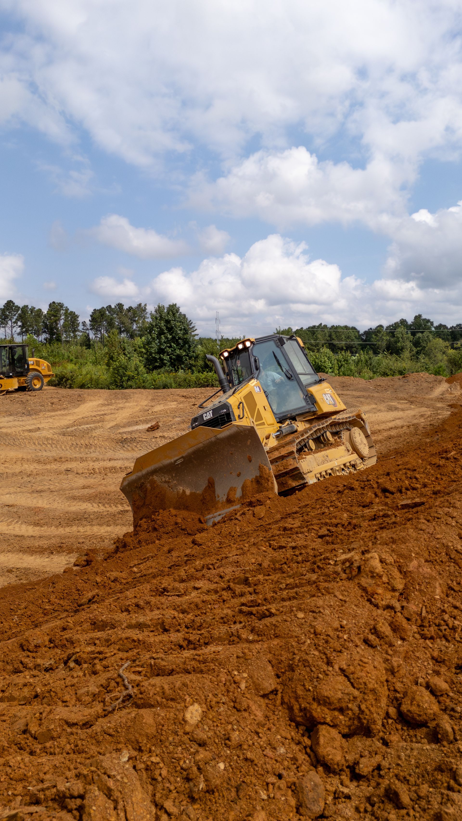 Bulldozer pushing brown earth on a construction site under a partly cloudy sky.