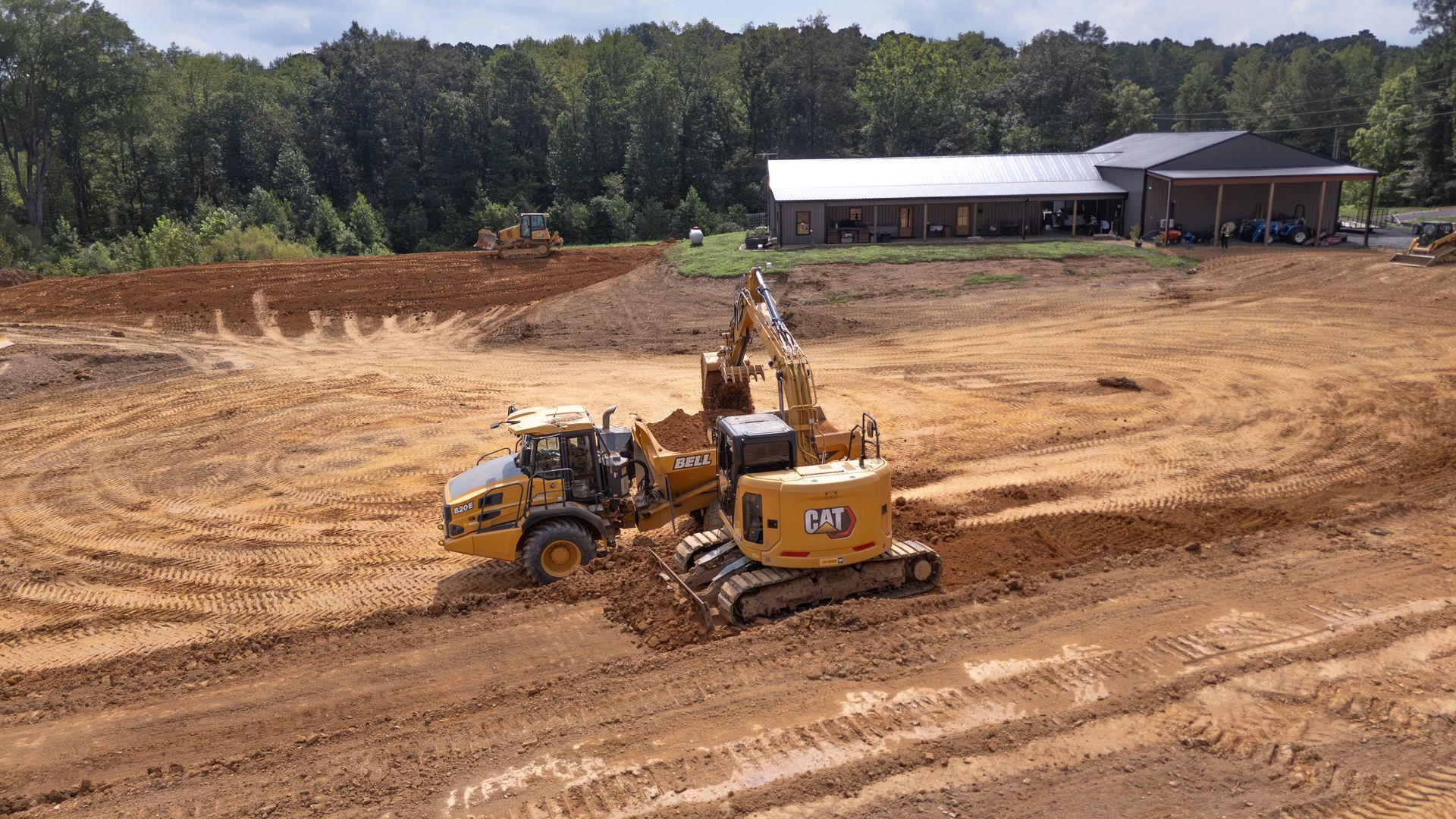 Construction site with heavy machinery grading land, building in background.