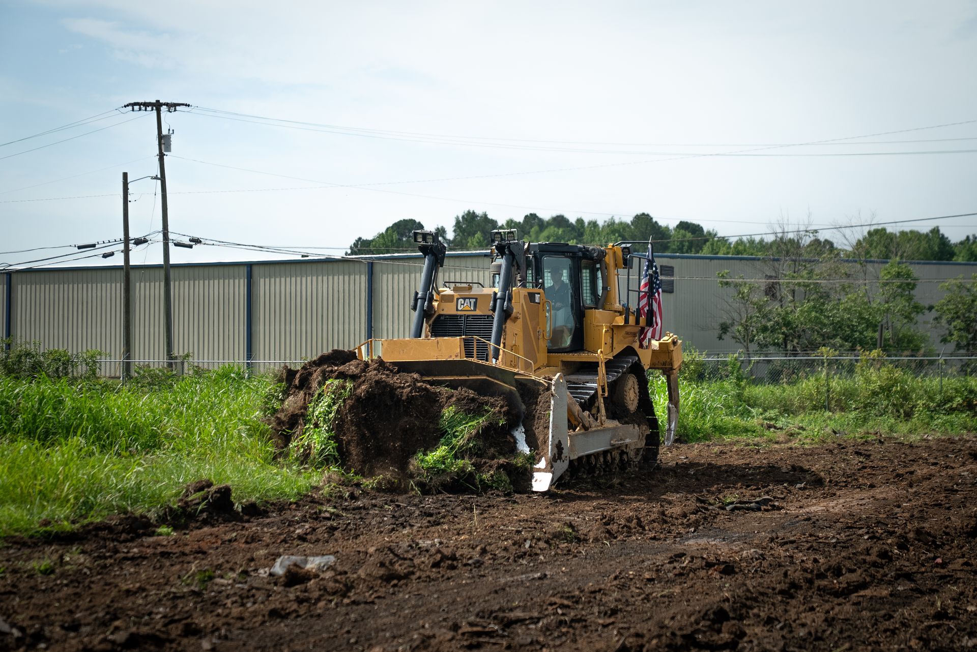 Yellow bulldozer pushing dirt in a field with tall grass and a fence.
