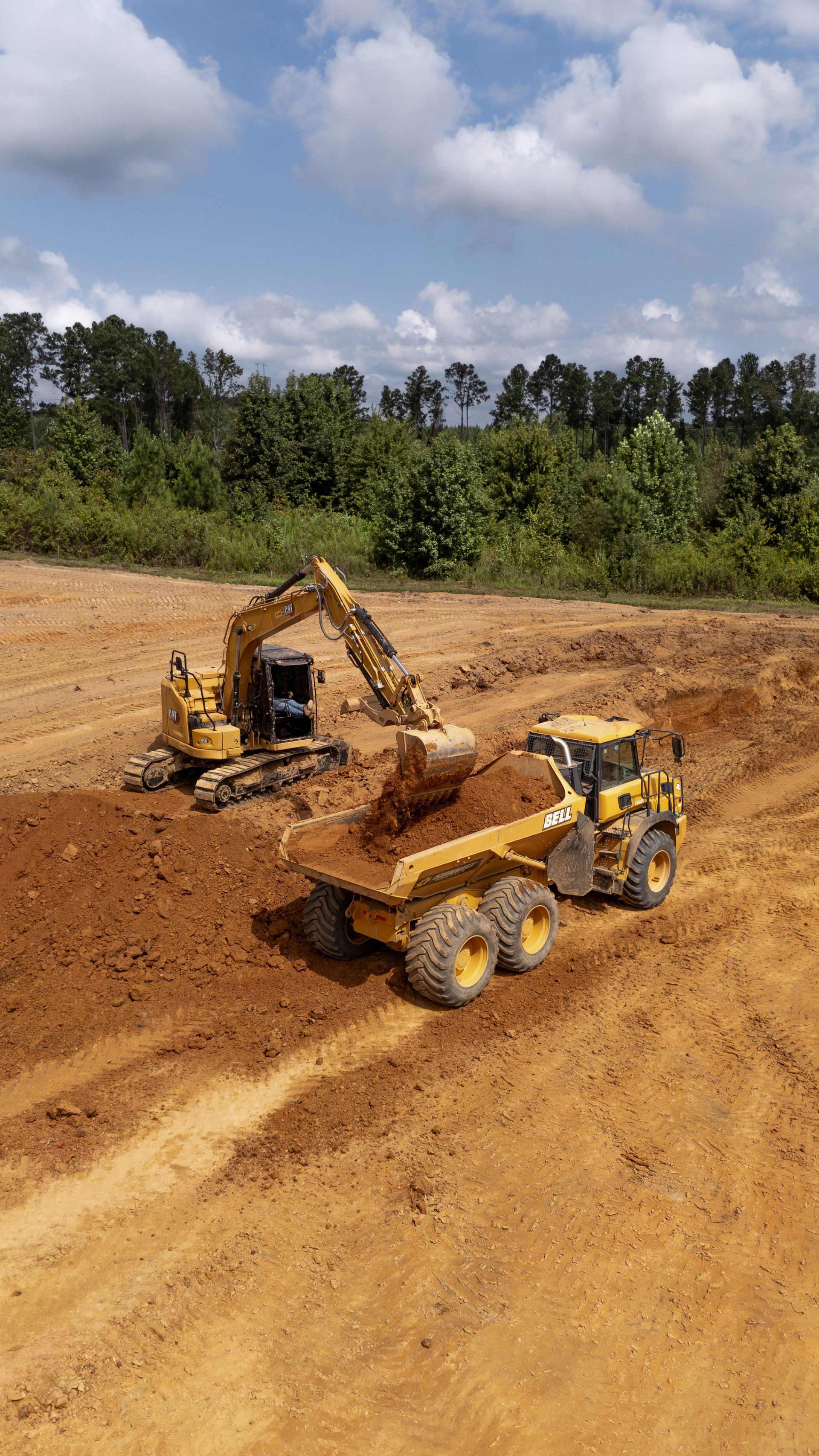 Excavator loading dirt into a dump truck at a construction site; trees in the background.