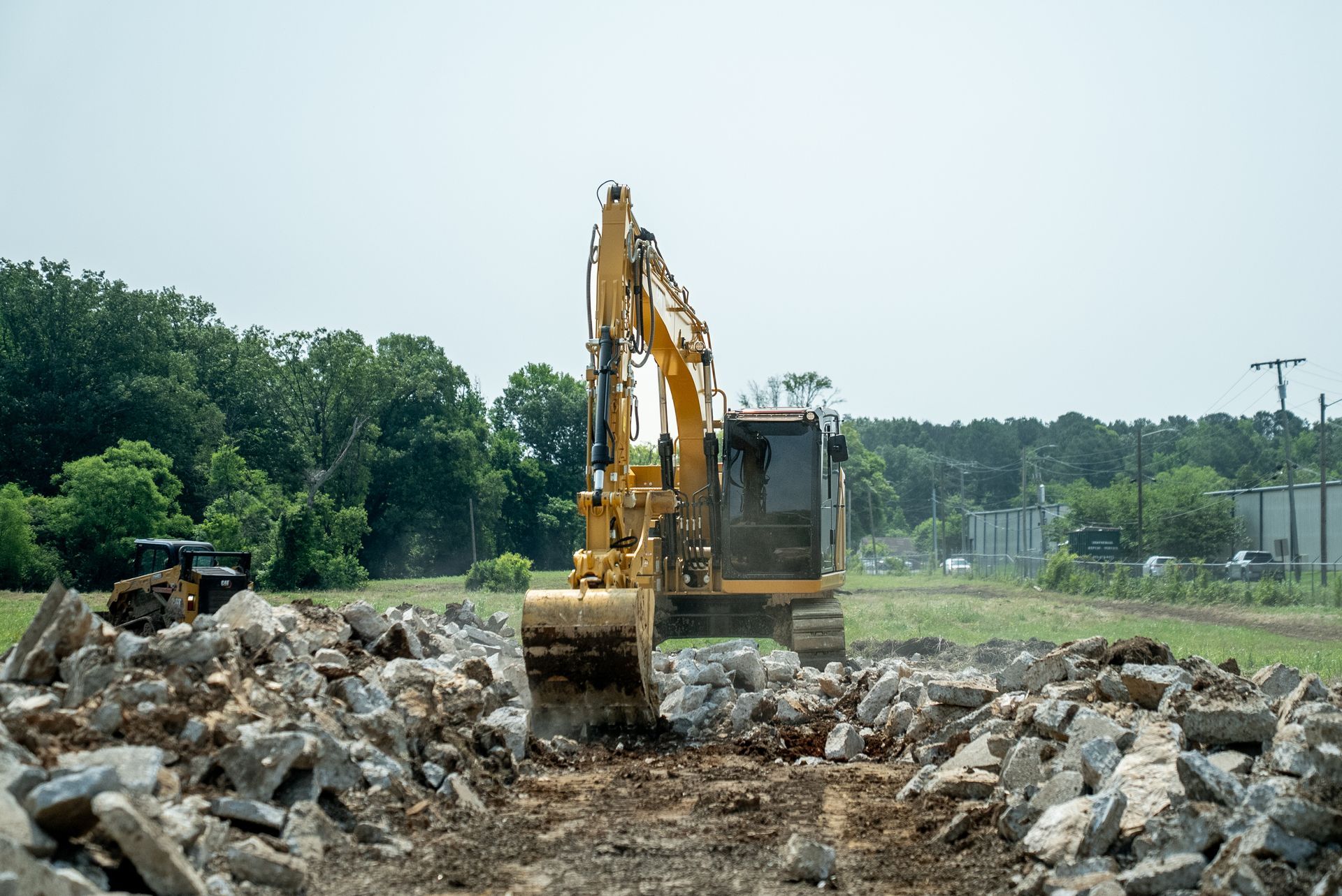 Yellow excavator moving concrete rubble on a construction site with trees in the background.
