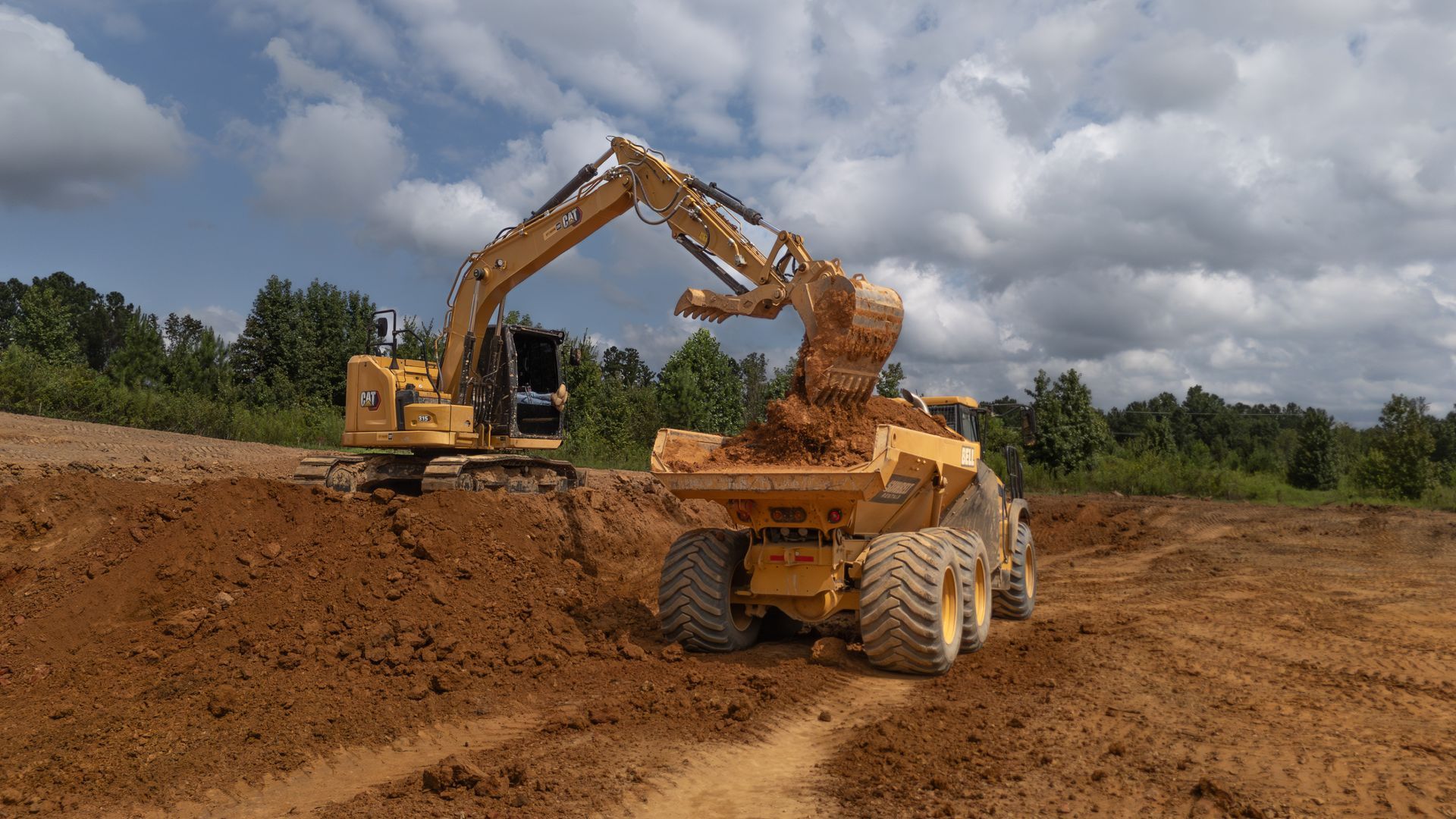 Yellow excavator loading dirt into a yellow dump truck on a construction site under a cloudy sky.