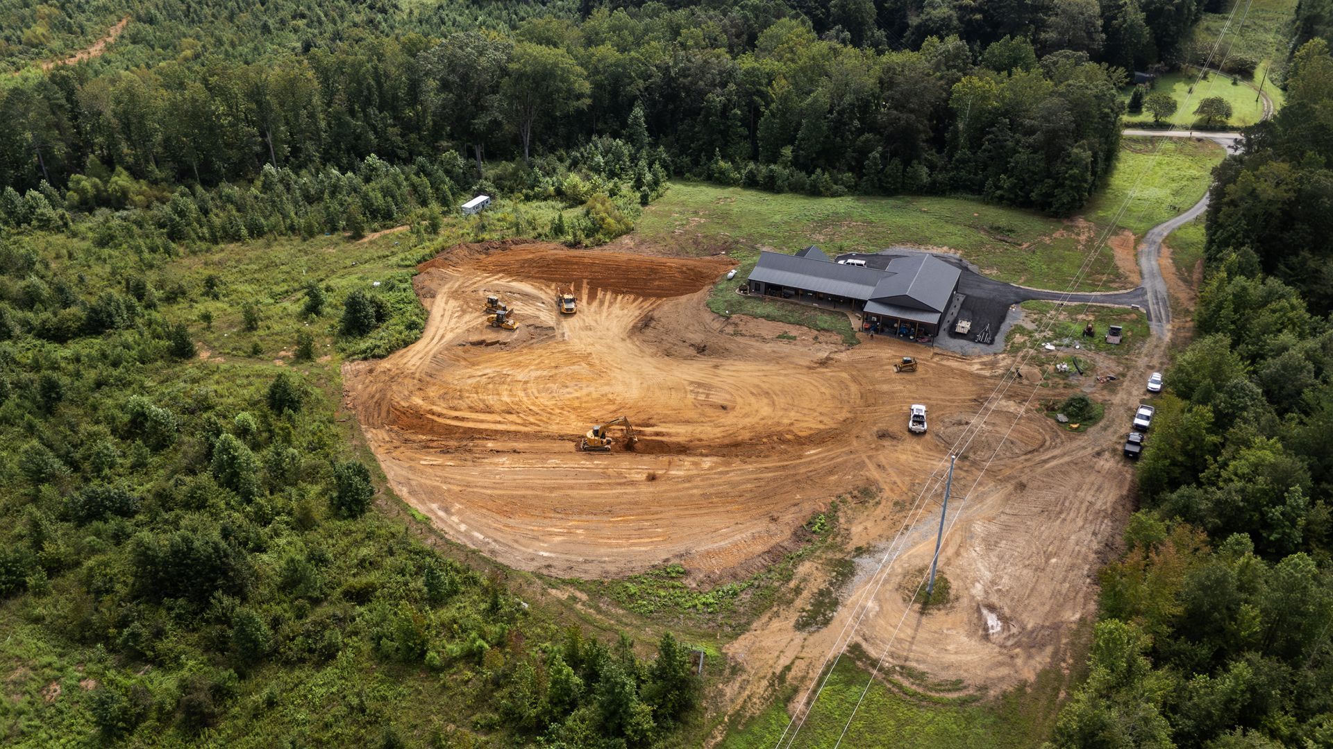 Aerial view of construction site with a partially built house surrounded by cleared land and forest.