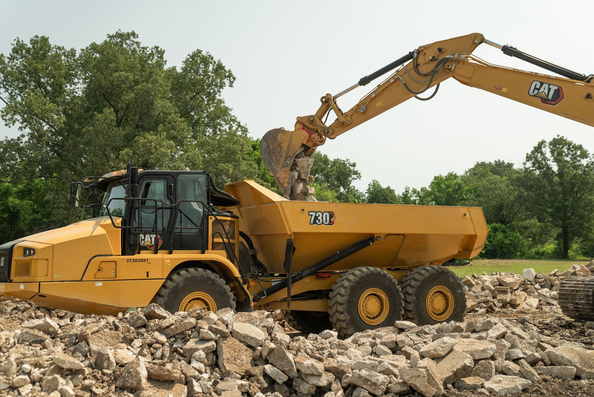 Yellow Caterpillar dump truck being filled with debris by an excavator.
