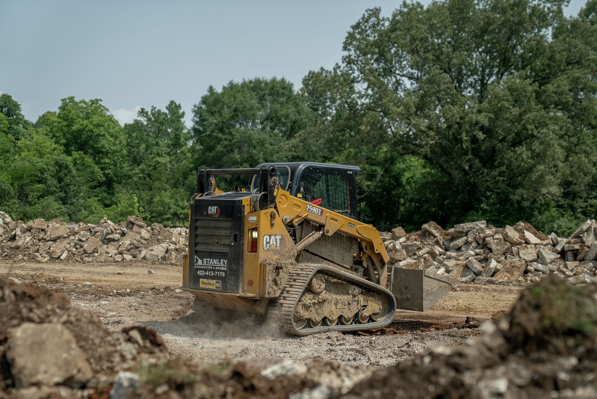 A yellow Caterpillar skid steer on tracks moves debris at a construction site.
