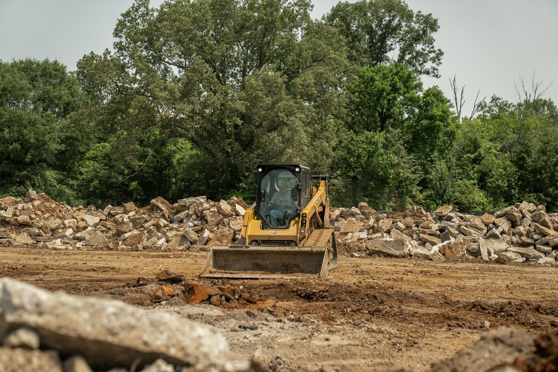 Yellow skid steer tractor moving dirt at a construction site.