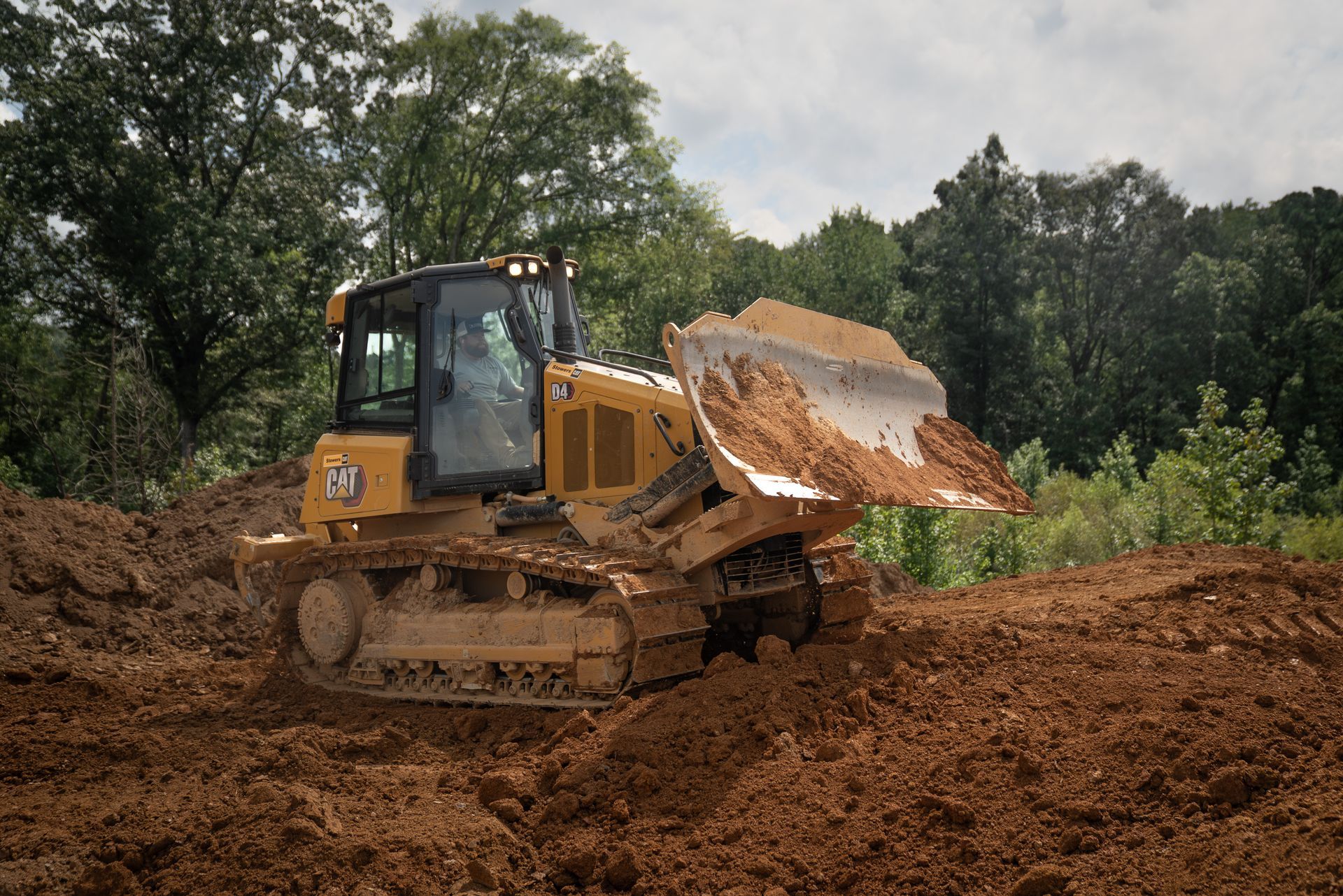 Yellow bulldozer pushing dirt in a wooded area.