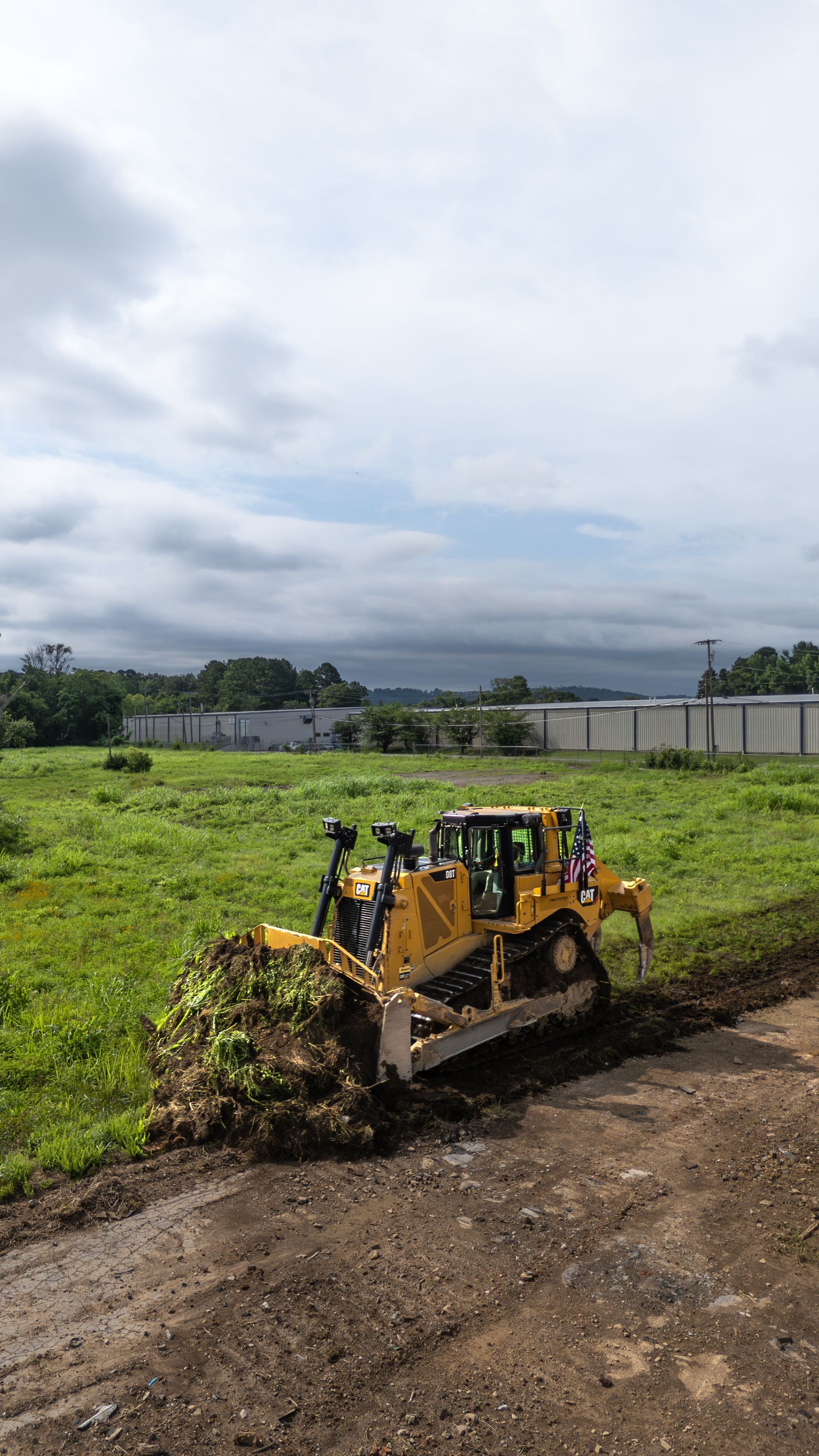 Yellow bulldozer clearing vegetation in a grassy field under a cloudy sky.