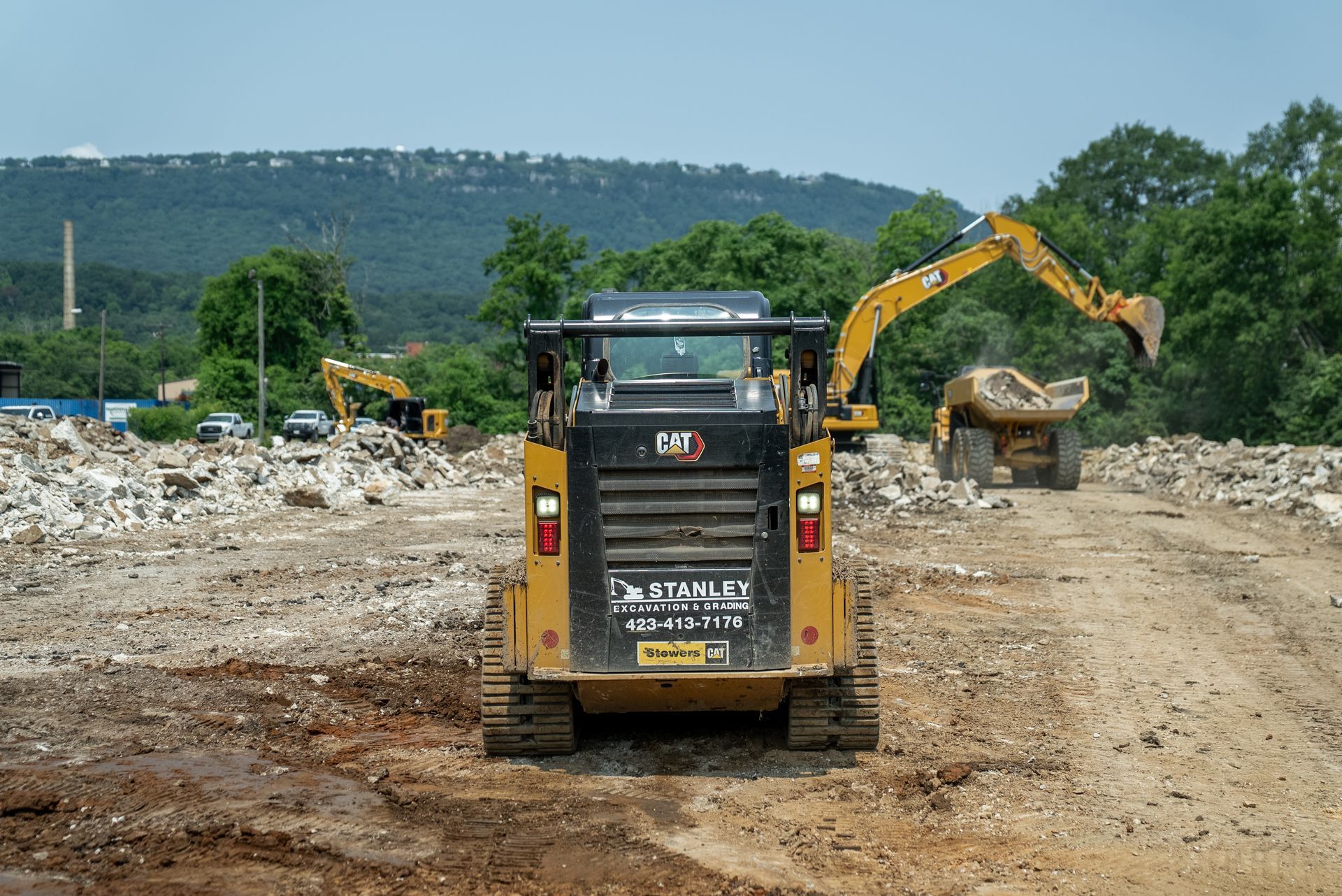 Yellow bulldozer on a brown mound of earth under a blue sky with clouds; another bulldozer in background.