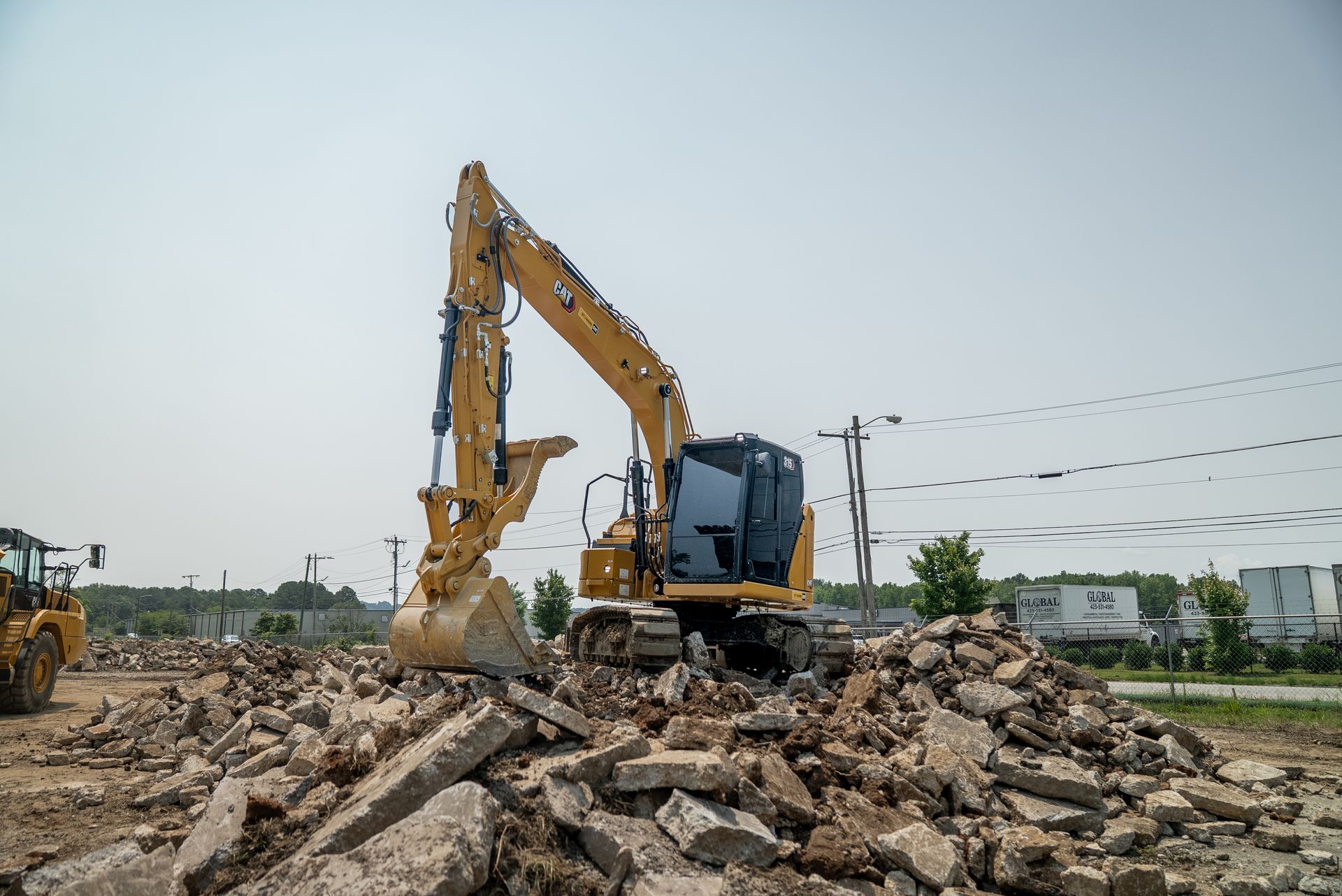 Yellow excavator demolishing concrete rubble outdoors under a clear sky.