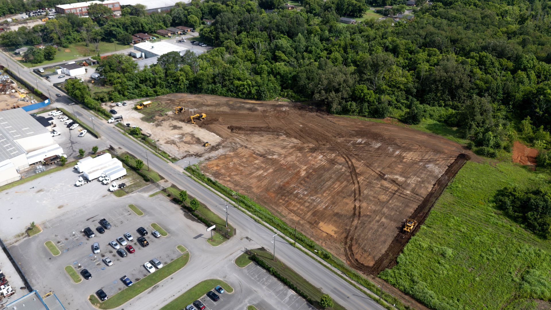 Aerial view of a cleared construction site next to a road, with heavy equipment and a parking lot visible.