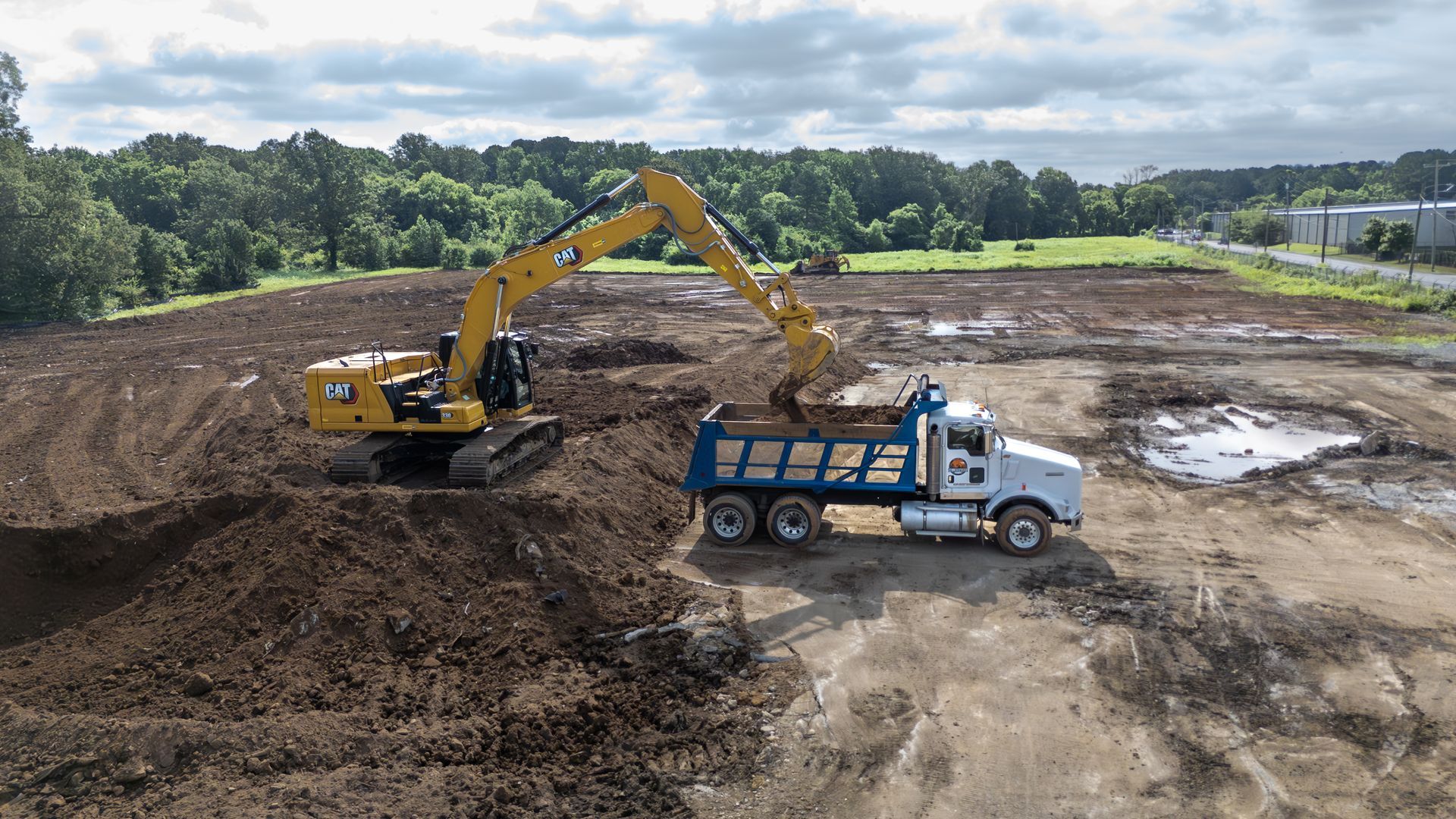 Yellow excavator loading a white dump truck with dirt on a construction site.