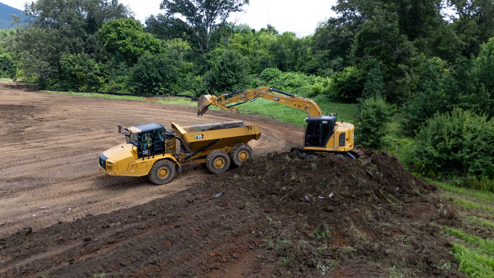 Excavator loading dirt into a yellow articulated dump truck on a construction site.
