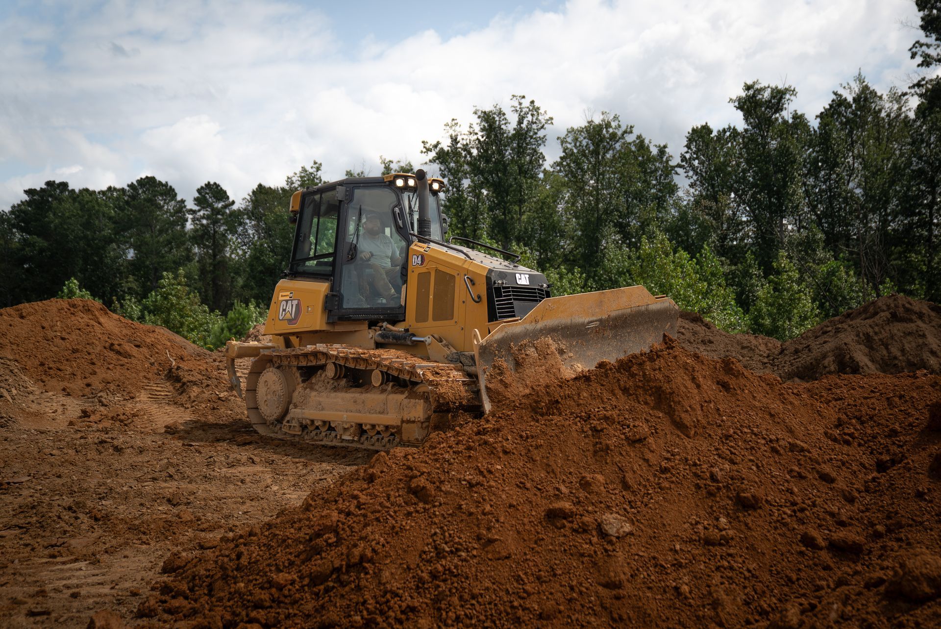Yellow bulldozer pushing brown dirt on a construction site with trees in the background.