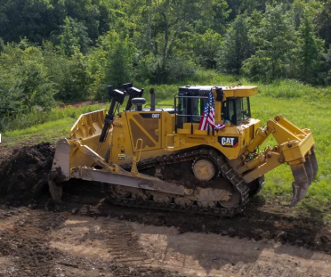 Overcast day with leafless trees and brown grass; snow falling over a gravel path and ditch.