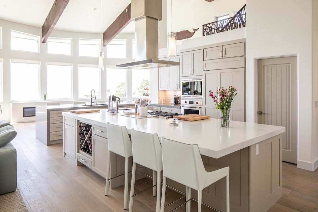 Modern kitchen with a large white island, three white bar stools, stainless steel appliances, and wood-paneled accents.